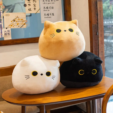 Three Velvet Plush Friend pillows by KittyNook Cat Co. in tan, white, and black stacked on a wooden table.